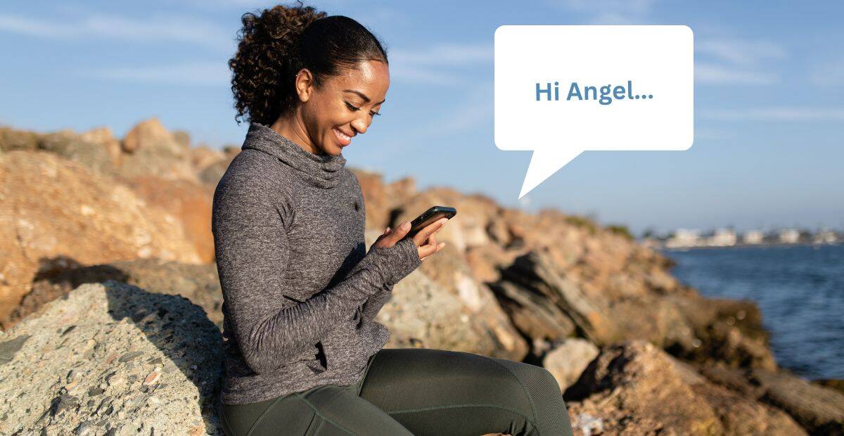 Best practices for SMS marketing | A female enjoying the beautiful sunset on a rocky beach, smiles as she reads a personalised SMS on her smartphone.