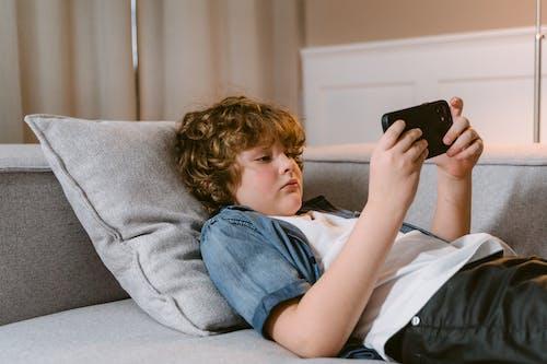 Free A Boy Using a Smartphone while Lying on a Sofa Stock Photo