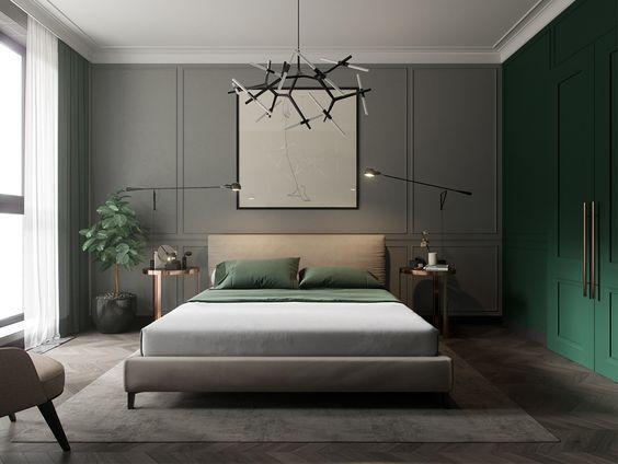 Quarto de casal com decoração verde e cinza, parede de fundo da cama cinza com molduras boiserie, piso reproduzindo madeira, armário verde, luminária com design moderna preta e vaso de planta