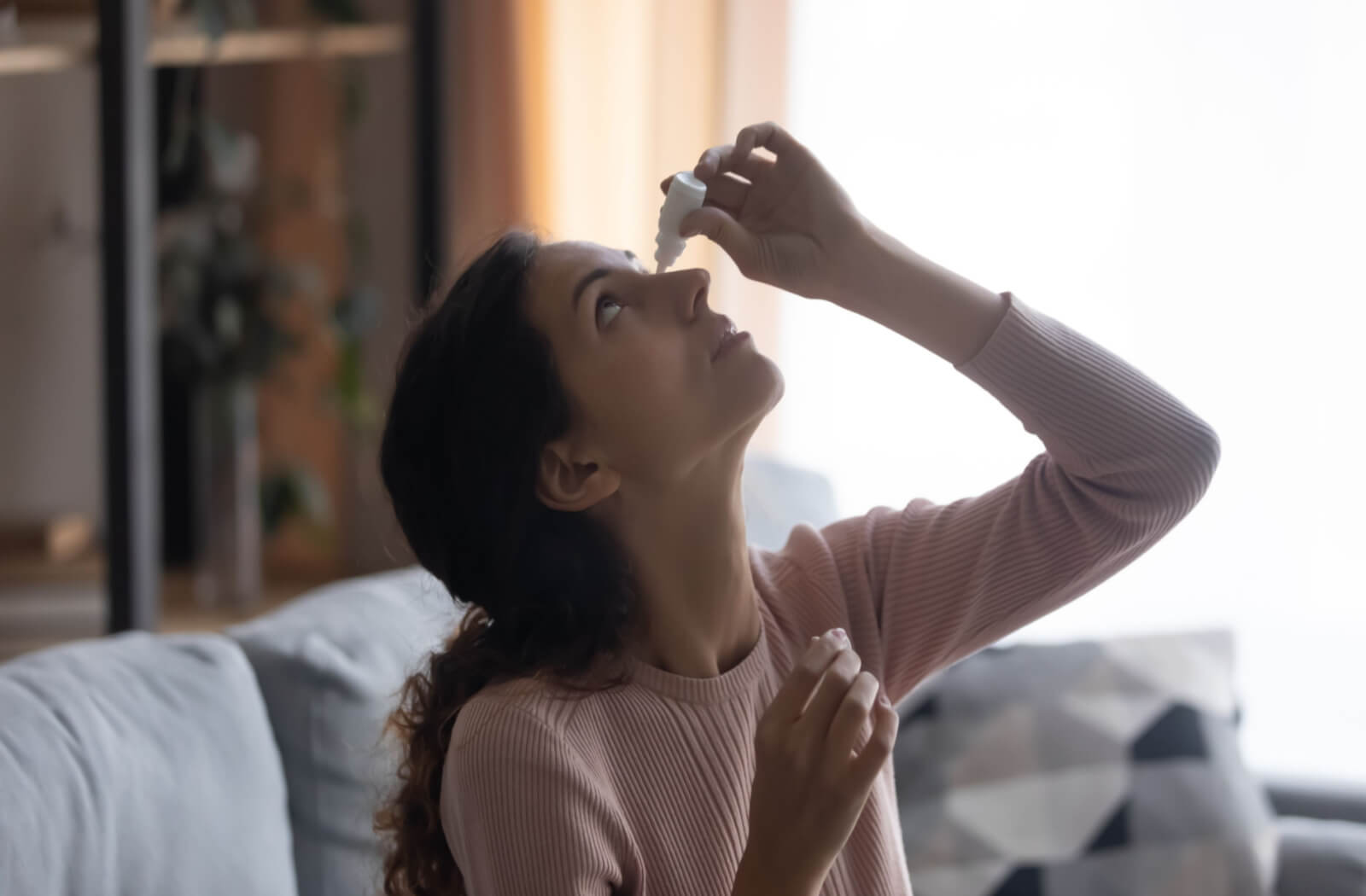 a woman applies eye drops to treat pink eye