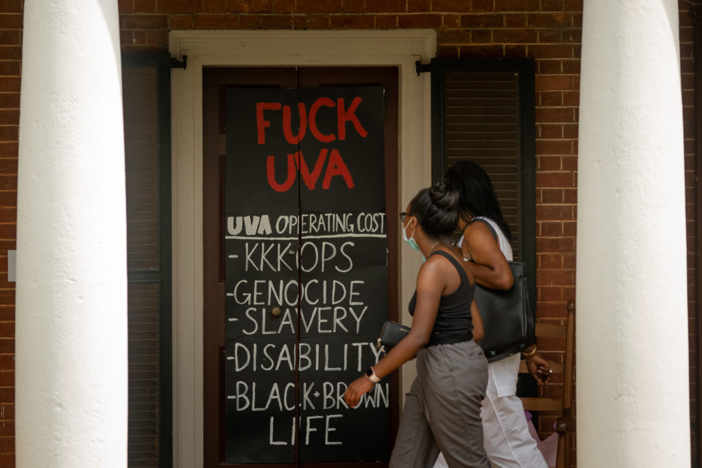 Two women walk by a door on a brick building with a sign that reads, "Fuck UVA."