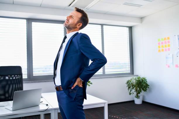 Lower back pain. Businessman stretches in office. Lower back pain. Businessman stretches in office. low back pain stock pictures, royalty-free photos & images