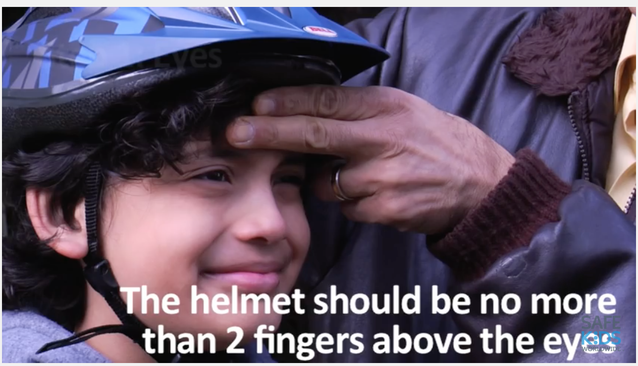 A close up of a boy getting his bike helmet fitted to the correct size with text below him.