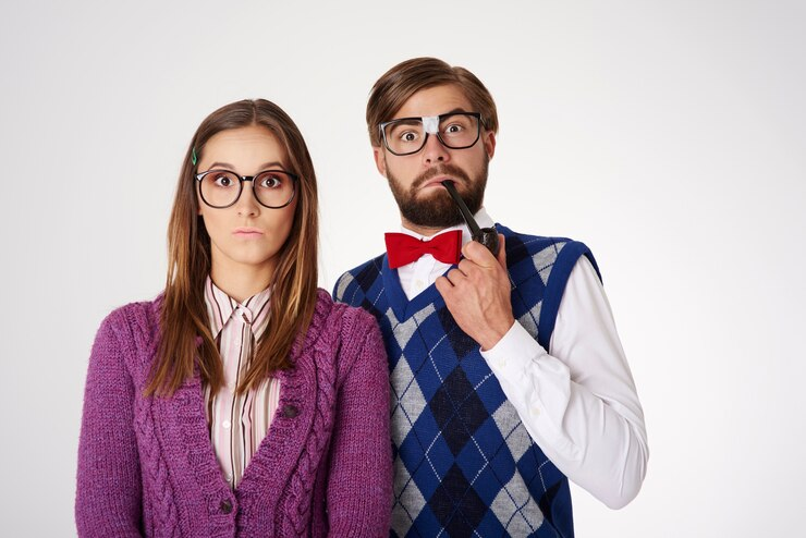 Fundo branco e casal ao centro vestindo roupas de frio coloridas e utilizando óculos, se assemelhando ao estereótipo do nerd. Foto: Freepik