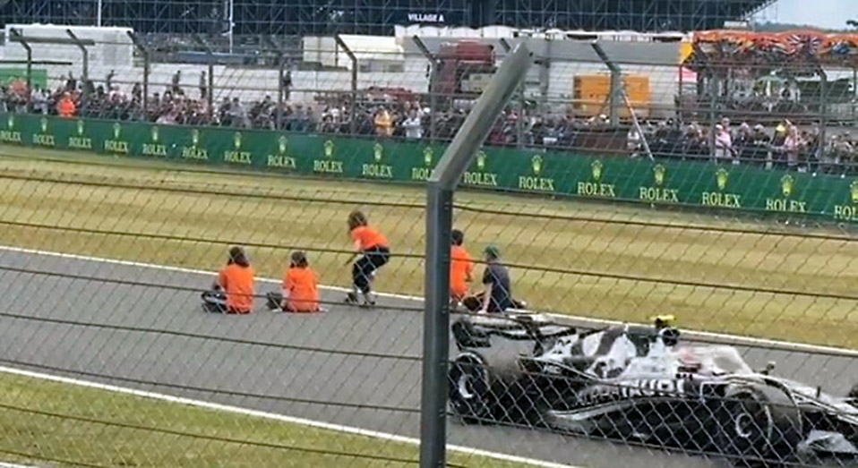 activists in orange shirts carefully kneel on the race track as an F1 car speeds by