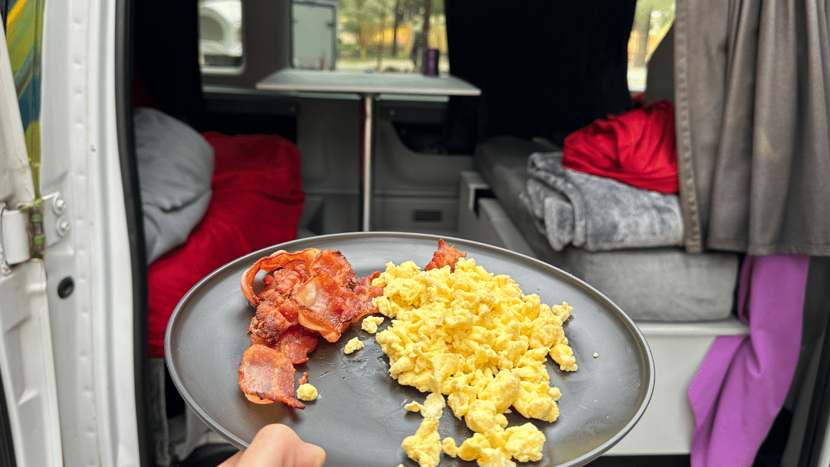 Eggs and bacon are on a plate in front of a table in the van