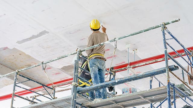 Painter painting roof while standing on a scaffold