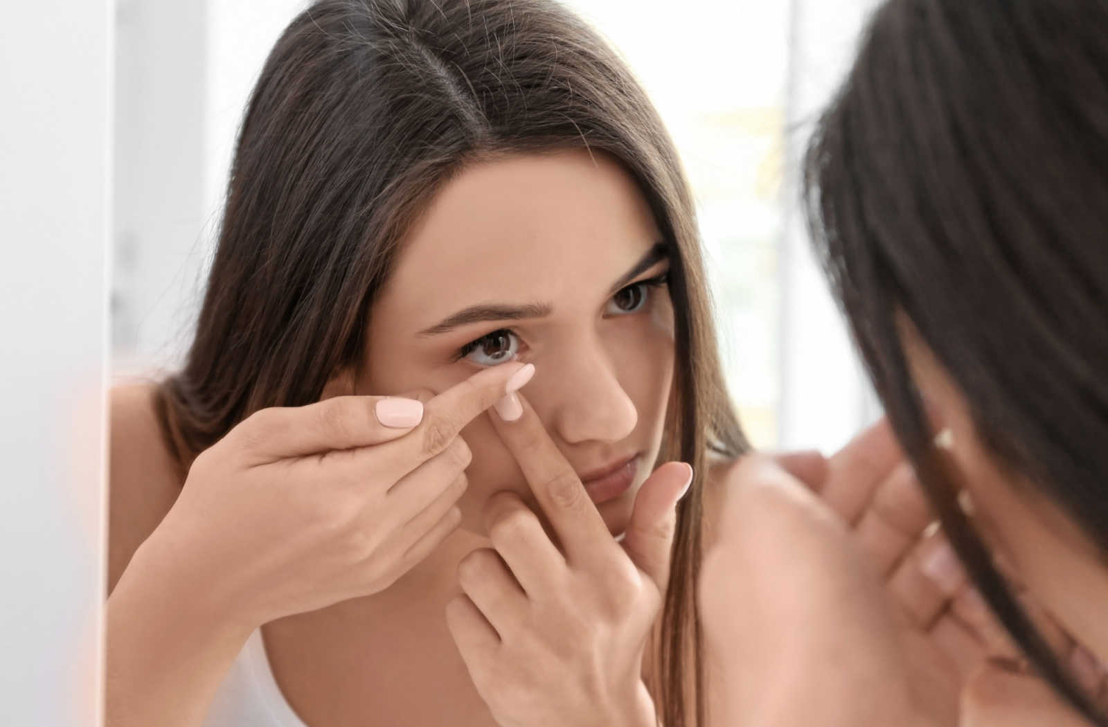 A woman applying a contact lens that does not worsen her dry eye symptoms.