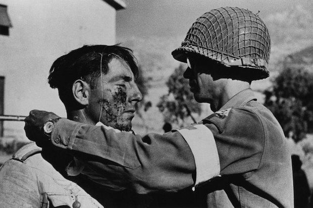 Two soldiers standing face-to-face. One has a wounded cheek that the other is tending to
