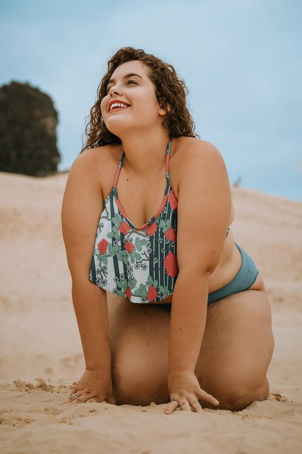 foto de uma mulher plus size de biquíni agachada na areia