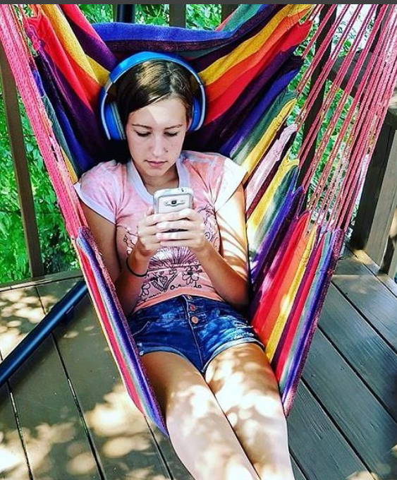 Young girl reading on her phone with headphones in summer outdoor swing