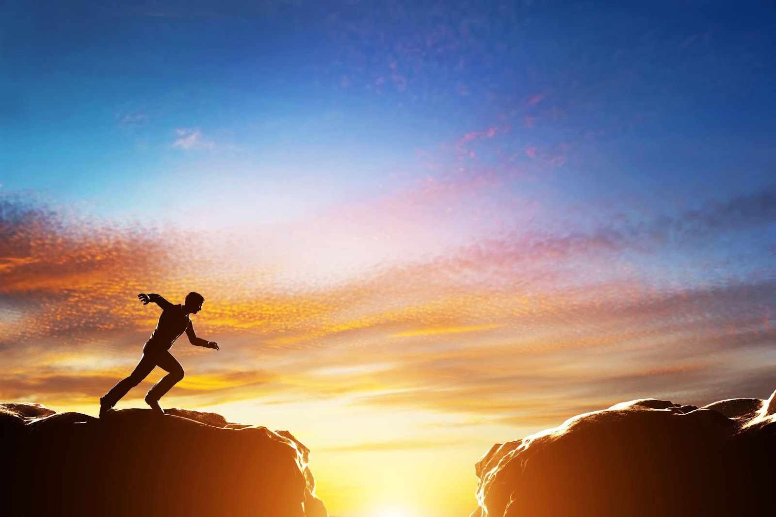 Person running fast to jump over precipice between two mountains