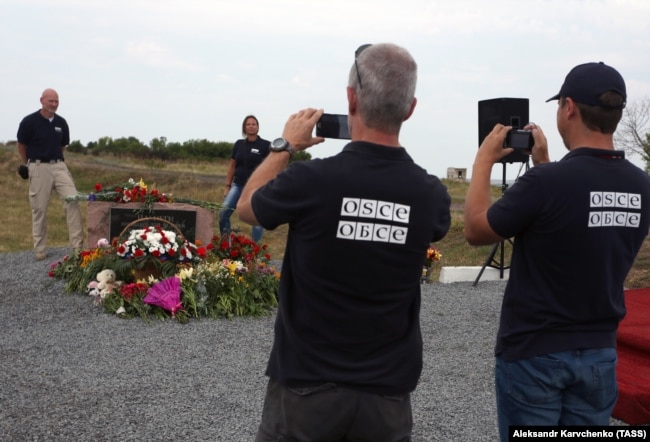 Сотрудники наблюдательной миссии ОБСЕ фотографируют мемориал погибшим в катастрофе рейса MH17 на месте крушения в третью годовщину трагедии, 17 июля 2017 года