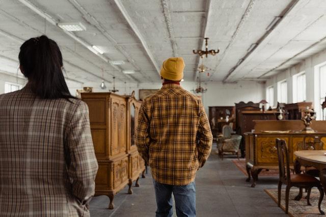 A woman and a man in plaid shirts walking around a vintage furniture store