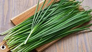 A bunch of green onions on a wooden board

Description automatically generated