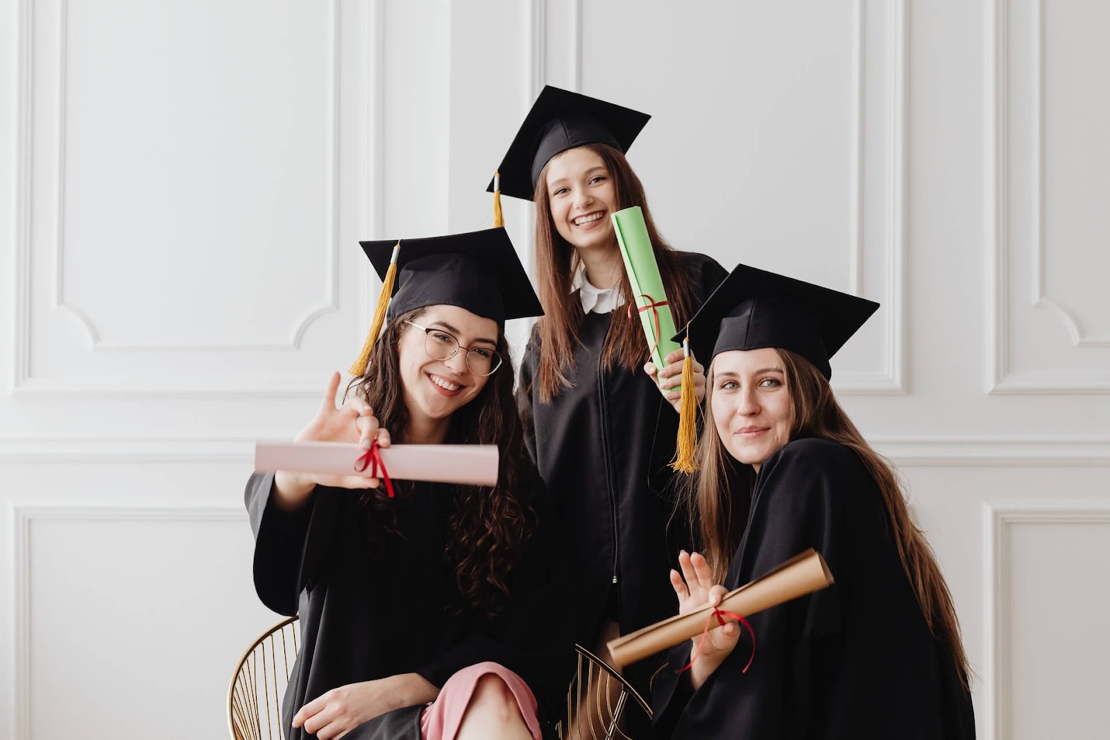 Three high school students holding their diplomas in their graduation robes