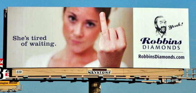 A Robbins Diamonds billboard with a woman holding up her ring finger and the message "She's tired of waiting."