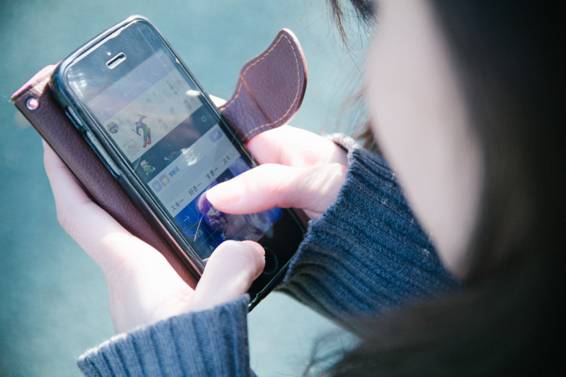 altテキスト：後ろ向きの女性がスマートフォンを両手で持っている
