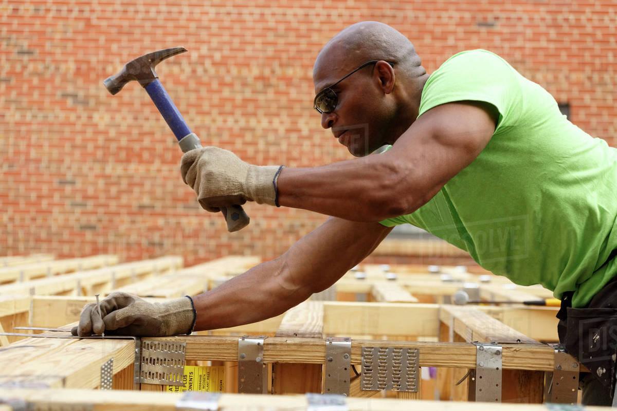 Black man hammering nail at construction site - Stock Photo - Dissolve
