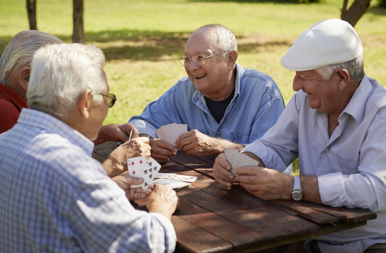a group of senior men play a card game at a picnic table outside in the sun