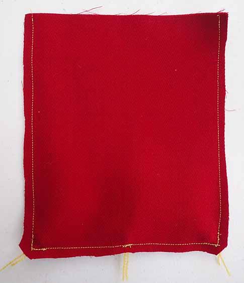Two pieces of red wool fabric sewn together with the corners clipped at approximately a 45 degree angle with three tassel cords visible along the bottom edge.