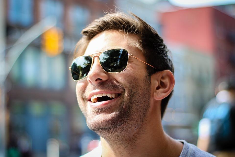 Man with brown hair wearing gold and black sunglasses smiling
