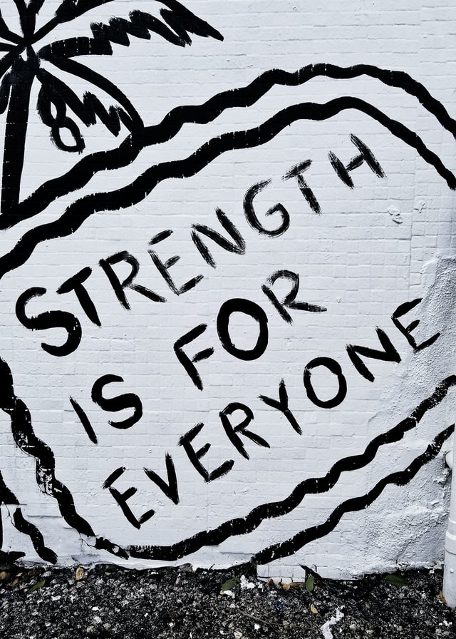 Graffiti on a wall reads "Strength is for everyone."