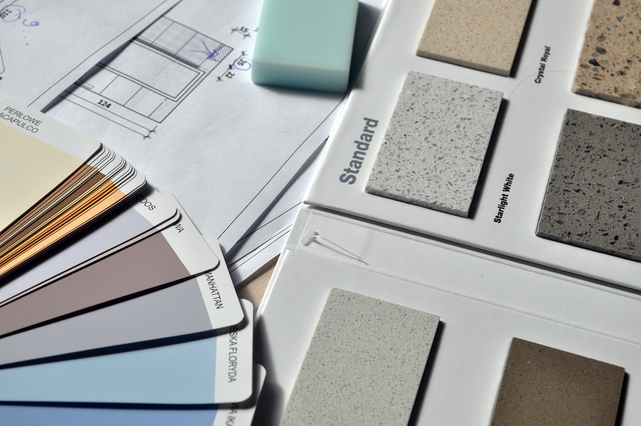 a flatlay of different countertop stone colour samples, paint sample colours, and blueprints for a renovation during the pandemic where supply chain issues faced home builders