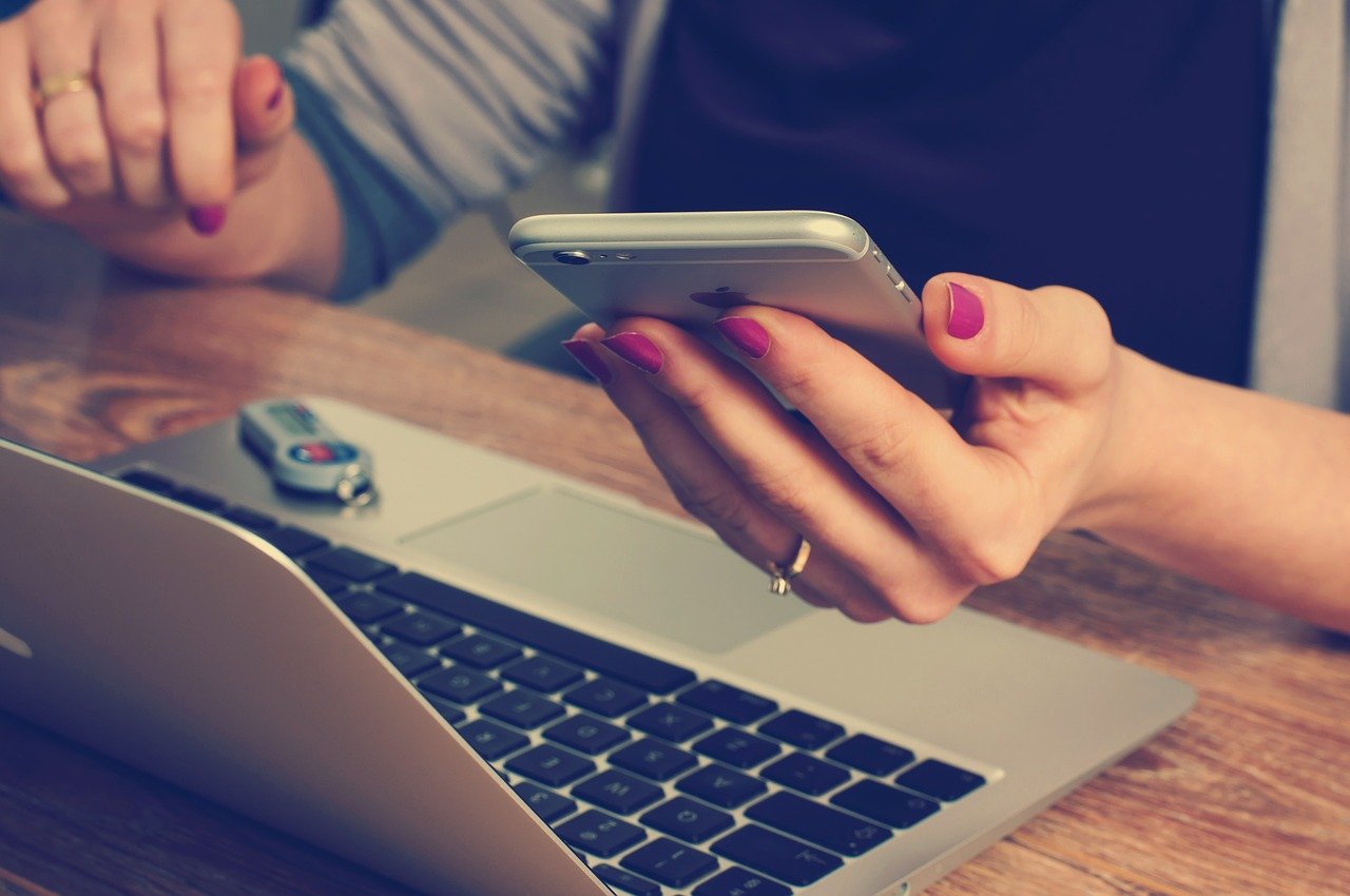 A woman sitting in front of a laptop and holding a mobile phone