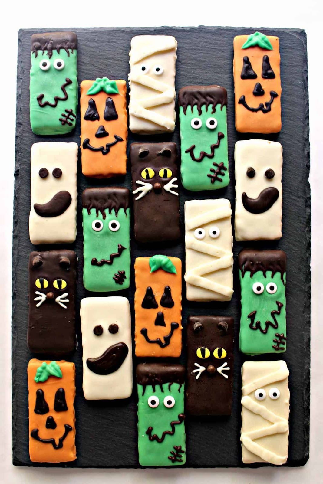 Graham crackers decorated with Halloween themed icing and monster faces on a black background.