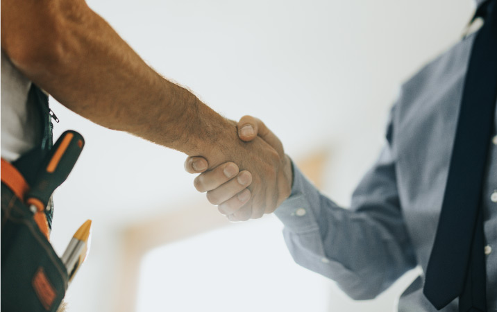 A man in a dress shirt and a tie shakes hands with the contractor he hired for his home remodeling project.