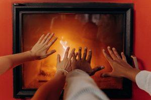 Two people warming their hands on the fireplace.