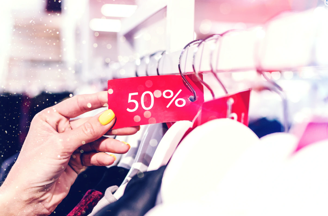 A woman's hand holding a 50% off tag at a clothing shop