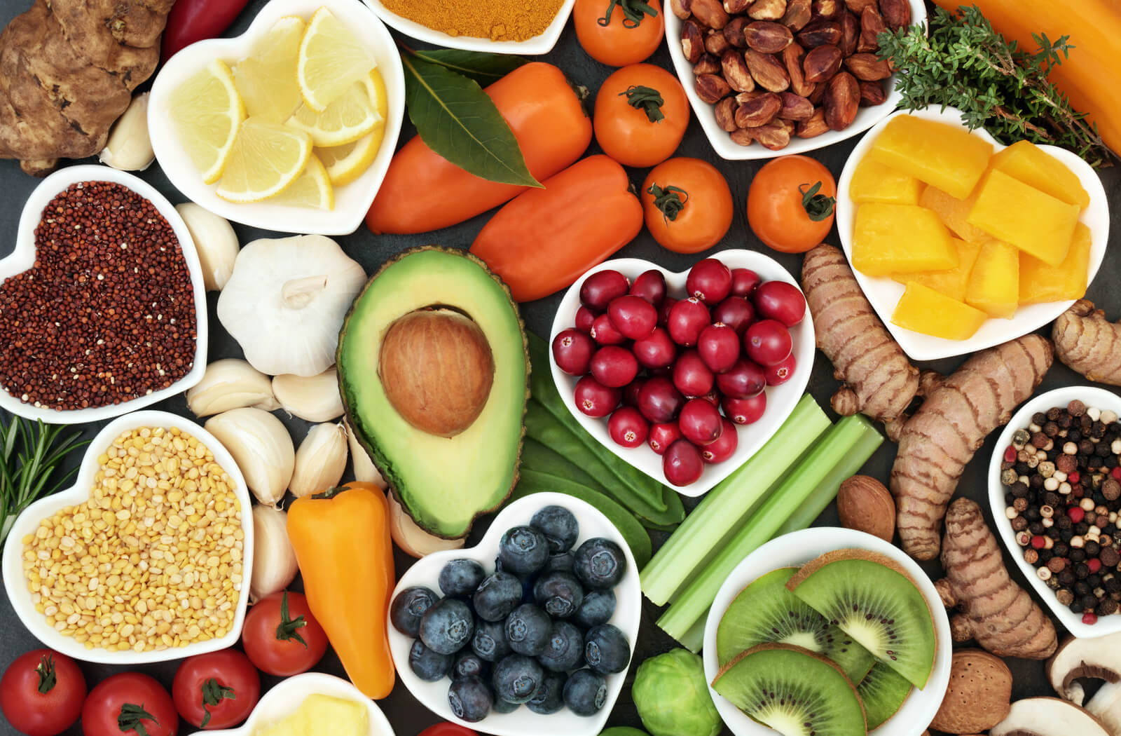 A picture of various fruits and vegetables from above including avocado, blueberries, lentils, peppers and tomatoes. some of the food is in heart-shaped bowls.