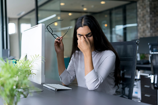 A woman sitting by her desk takes her glasses off and rests her face on her hand. This photo could represent a person experiencing anxiety. Anxiety treatment in Los Angeles, CA can help with coping skills by talking to an anxiety therapist. | 93020 | 94513 91356 | 91020