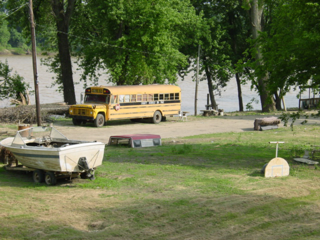 School bus used as a home, with mowed lawn around it on the bank of a river
