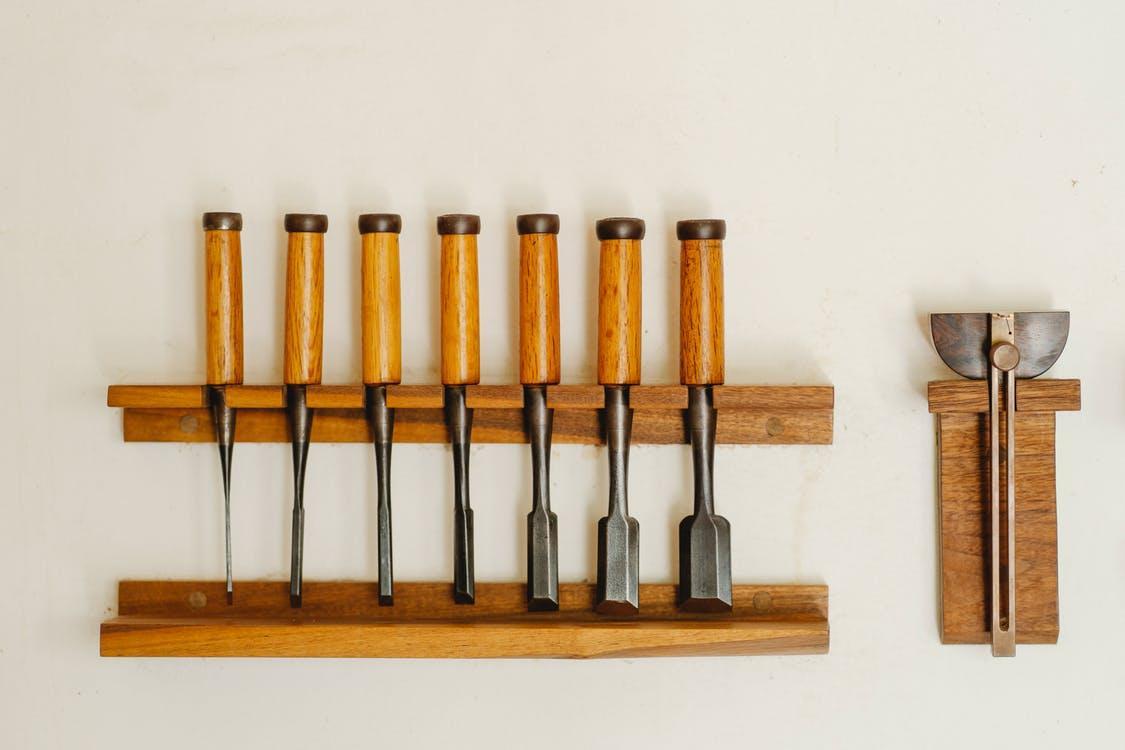 Collection of metal chisels with wooden handles and wood cutters for woodwork arranged on shelf on white wall in workshop