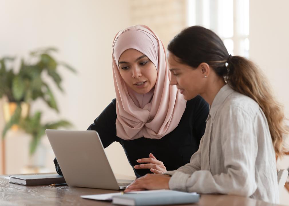 Young arabian woman in hijab sitting with smiling colleague at table