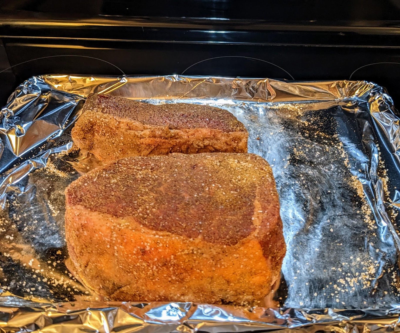 Two beef roasts seasoned and sitting on a foil lined sheet pan