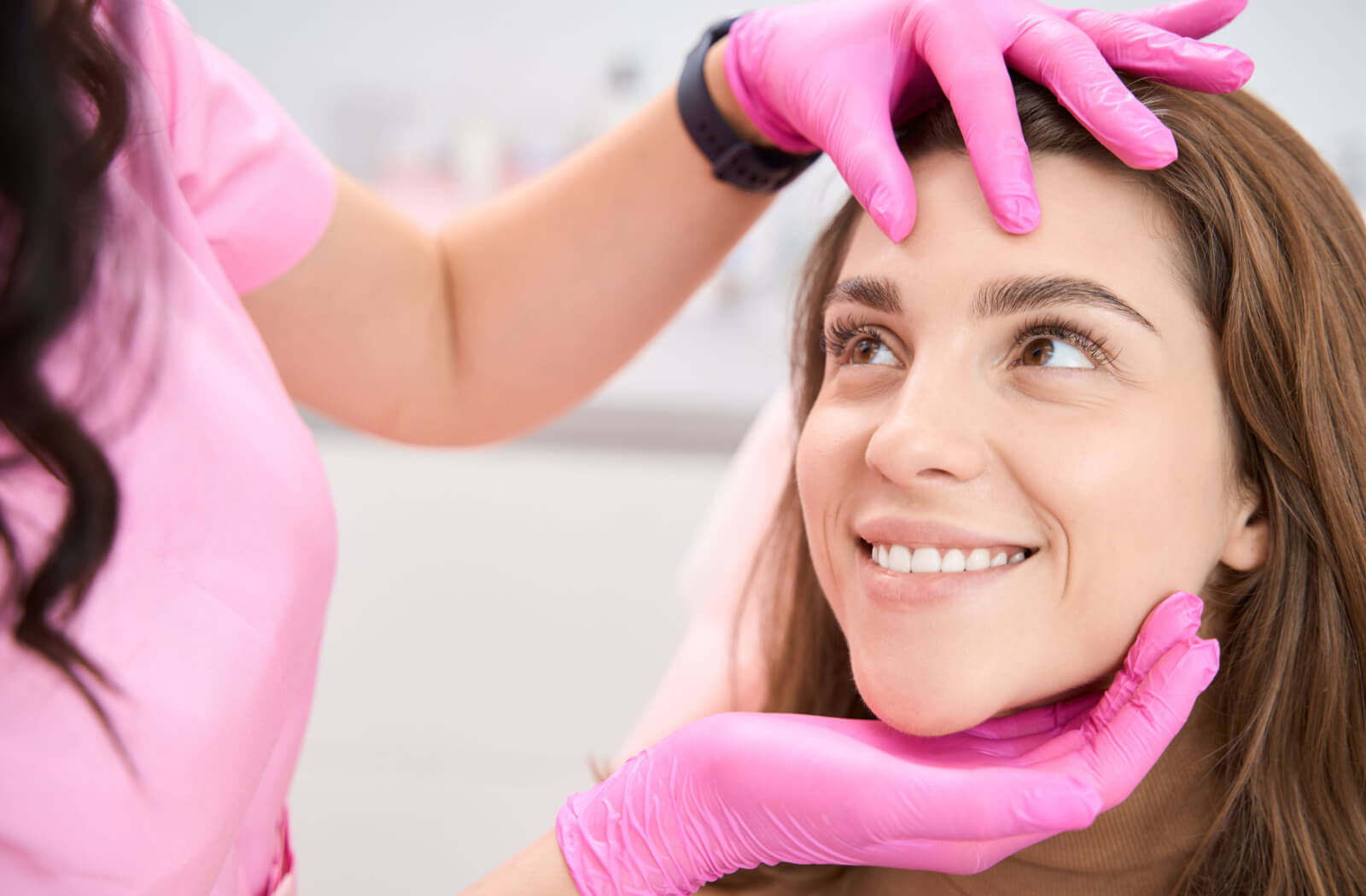 A woman smiling while being professionally examined by a cosmetologist.