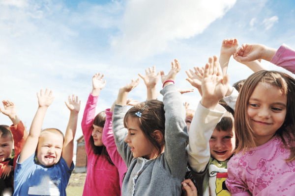 Group of preschool children outside, raising their hands in the air.