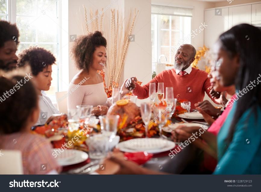 Multi generation mixed race family holding hands and saying grace before eating at their Thanksgiving dinner table, selective focus