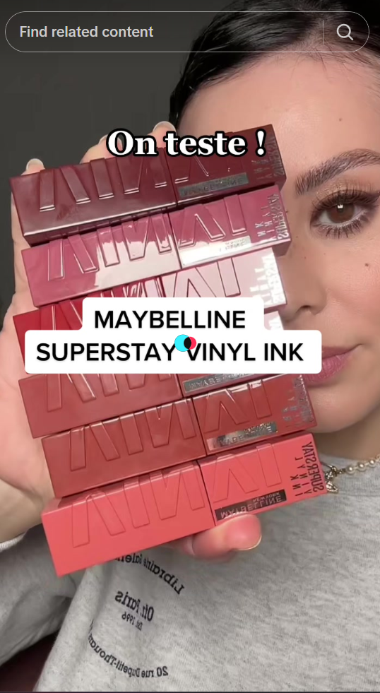 A screenshot of a woman on social media showing make up products and some texts in the middle saying "maybelline superstay vinyl ink"