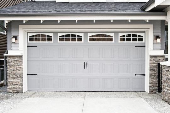 WeServe |  a wide grey garage door with windows and black handles with a grey roof and a marveled driveway