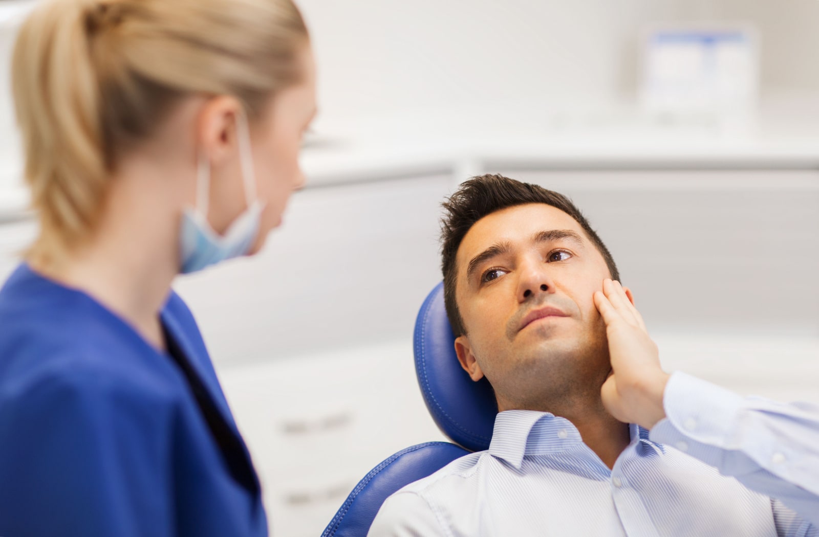 A man sitting back in a dental office chair, discussing his tooth pain with a female dentist