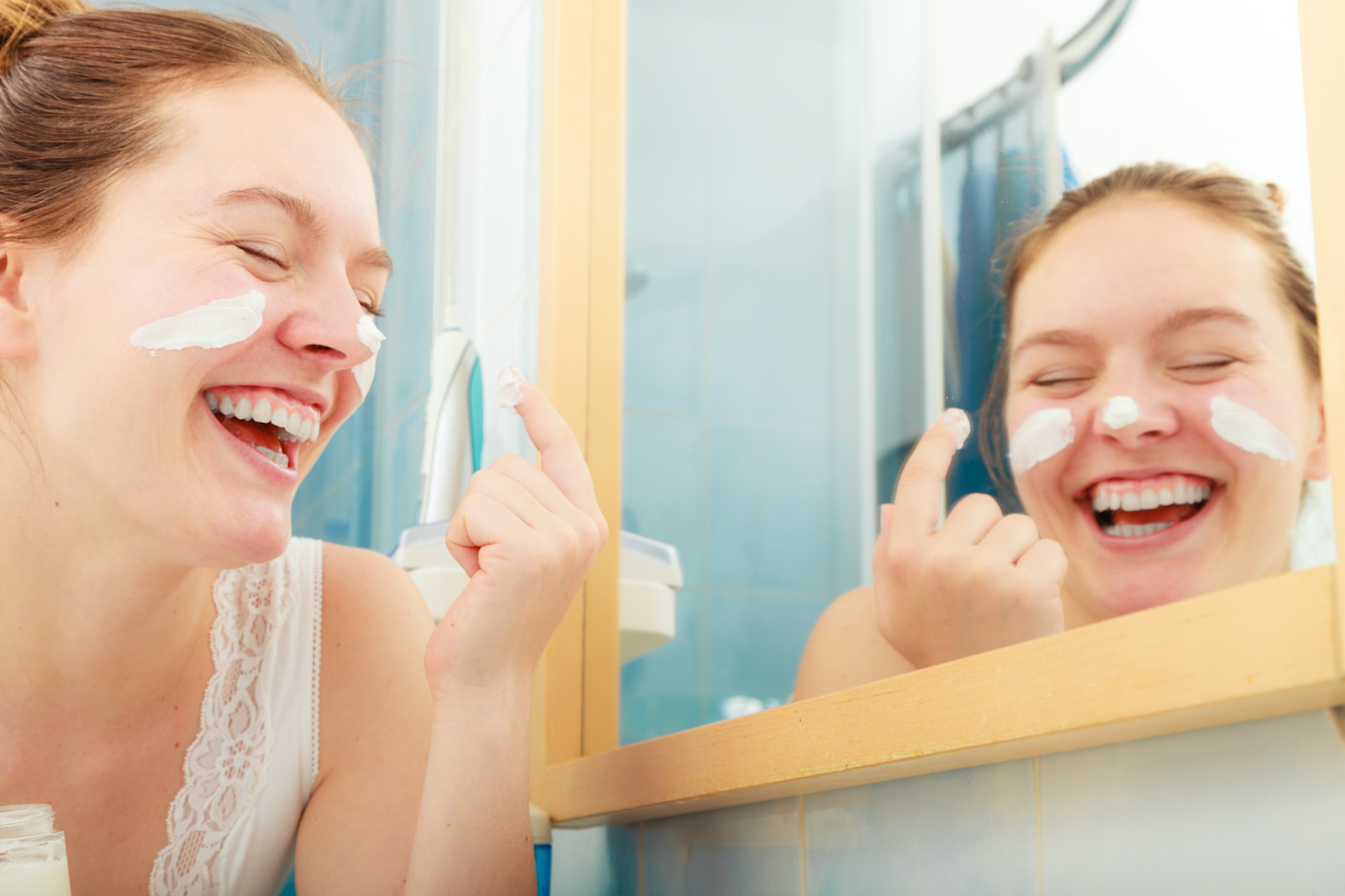 mulher com expressão sorridente enquanto passa um produto para hidratar a pele