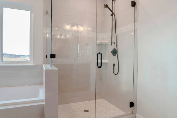 Bathroom shower stall with half glass enclosure adjacent to built in bathtub Bathroom shower stall with half glass enclosure adjacent to built in bathtub. The window offers a scenic view of snowy winter landscape and cloudy sky. shower enclosure stock pictures, royalty-free photos & images