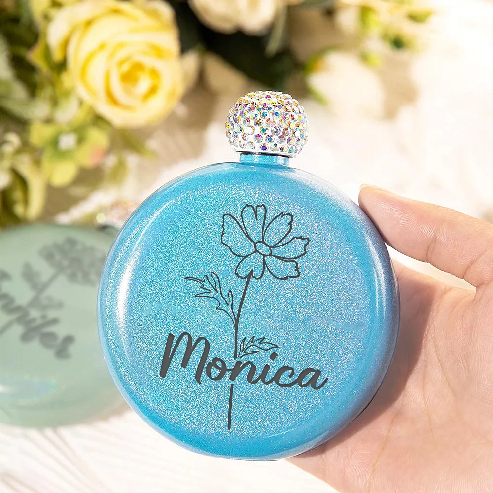 bouteille de parfum bleue personnalisée avec une fleur et un prénom et surmontée d’un bouchon perlé.