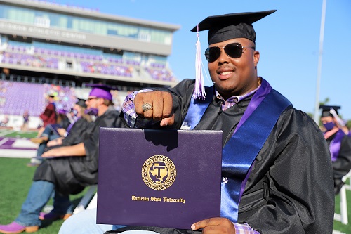Photo of student graduating and showing off alumni ring