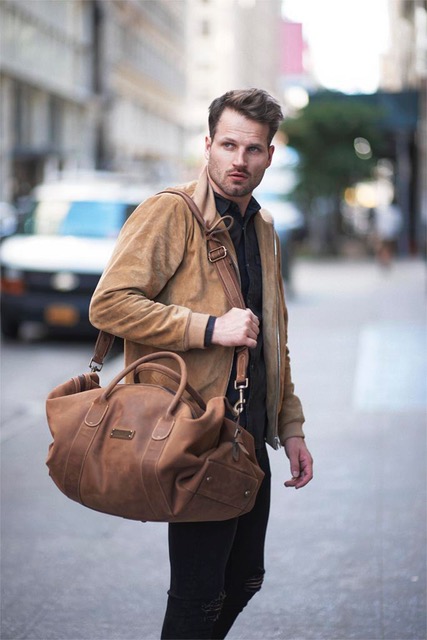 Another editorial image by Steve. A young man in a leather jacket stands in the street with a duffel bag over his shoulder.